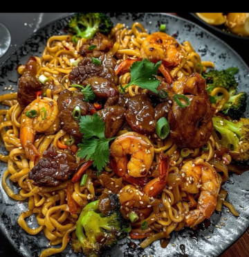 Plate of shrimp and beef stir-fry with noodles, broccoli, sesame seeds, and cilantro garnish