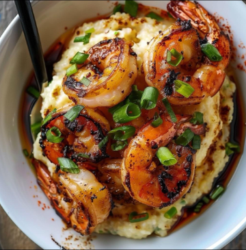 Grilled shrimp seasoned with spices on creamy grits topped with chopped green onions in white bowl
